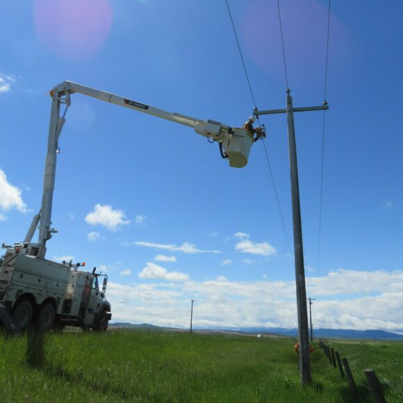Outdoor photograph of a bucket truck lifting a worker within reach of a transmission tower