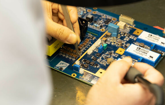 Closeup photograph of worker soldering parts onto a reverse engineered circuit board