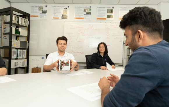 Workers in a boardroom handling a small machine part that is being reverse engineered