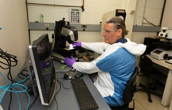 A worker in protective suit operating digital microscope