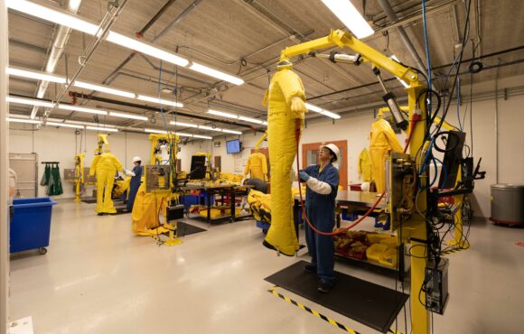 Workers mounting protective suits into testing apparatus