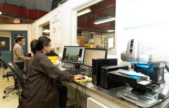 Workers observing microscope samples through a computer monitor