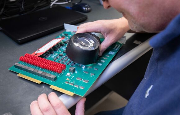 Worker examining circuit board through a magnifying glass