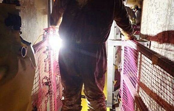 Worker wearing protective equipment, walking across a dark catwalk