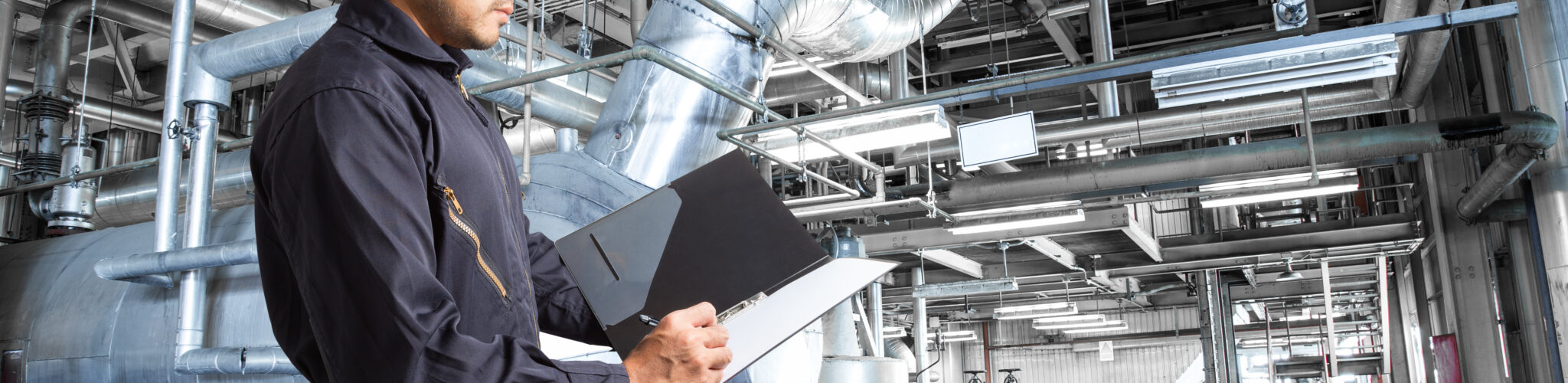 Worker with clipboard examining large facility equipment