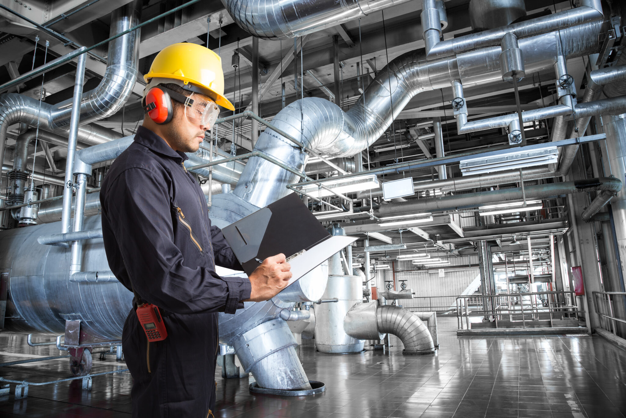 Worker with clipboard examining large facility equipment