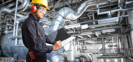 Worker with clipboard examining large facility equipment